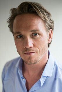 a close up of a person wearing a blue shirt and looking at the camera with a serious look on his face