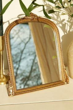 a mirror sitting on top of a table next to a vase