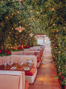 the inside of a restaurant with tables and chairs covered in greenery, lit by hanging lights