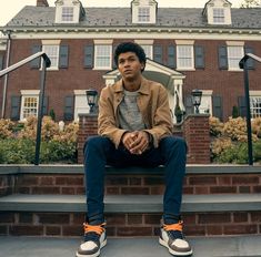 a young man sitting on the steps in front of a large brick building with stairs leading up to it