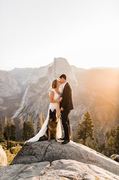 a bride and groom kissing on top of a mountain with their dog in the foreground