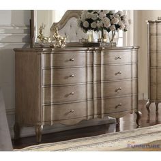 a dresser and mirror in a room with white flowers on the top, gold accents