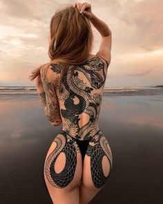 a woman is standing on the beach with her back to the camera and tattoos on her body