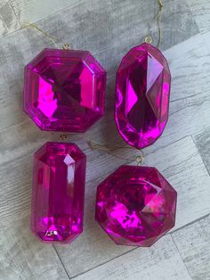 three bright pink jeweled ornaments on a wooden surface, one is hanging from a gold chain