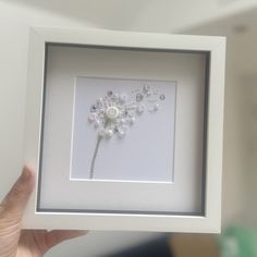 a person holding up a white frame with flowers in it and pearls on the side