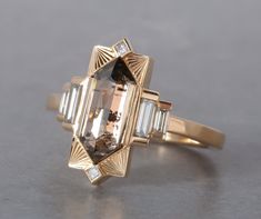 Named after Hilma AF Klint. This new setting was a dream ring we had been envisioning in the back of our minds for some time. For our first ring we chose this lovely 1.74ct Champagne Rosecut Elongated Hexagon Diamond and we accented it with some good size diamond baguettes and a few princess diamonds on the top and b Saphire Engament Ring Bezel, Art Deco Fine Jewelry, Art Deco Ring Vintage, Architectural Engagement Ring, Artemer Engagement Rings, Elongated Hexagon Ring, Dream Engagement Rings Gold, Alternative Stone Engagement Rings, Elongated Hexagon Engagement Ring