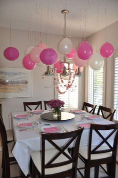 a dining room table with pink and white balloons hanging from the ceiling