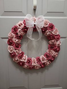 a wreath made out of rolled up pink and white roses with a bow hanging on the front door