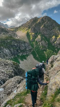 people hiking up the side of a mountain with backpacks on their back and one person walking