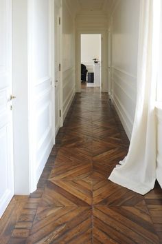 an empty hallway with wooden floors and white walls, leading to another room in the house