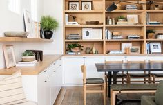 a wooden table sitting next to a bookshelf filled with lots of books and plants