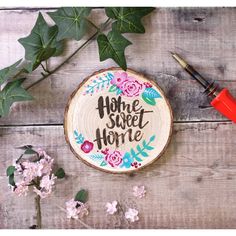 a wood slice with the words home sweet home painted on it next to some flowers