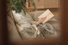 a woman laying on a couch reading a book with her hands resting on the pillow