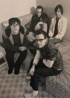 an old black and white photo of four men sitting on a bed in a room