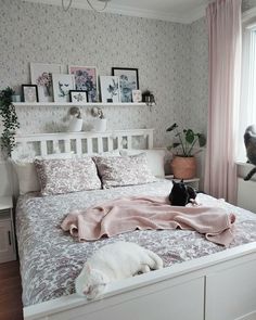 a cat laying on top of a bed in a room with pink curtains and wallpaper