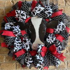 a cow wearing a red, black and white mesh wreath on a brick wall in front of a brick building