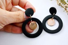 a pair of black and gold hoop earrings on top of a white table next to flowers