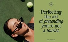 a woman laying on top of a tennis court next to a green wall with a quote about perfecting the art of pretending you'ret not a tourist