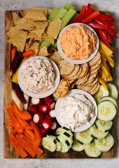 a platter filled with crackers, vegetables and dips