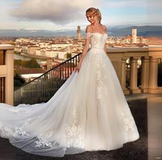 a woman in a white wedding dress standing on a balcony with her hand on her hip