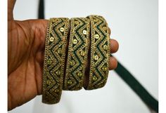 a hand is holding three bangles with gold and green designs on them, all in different shapes and sizes