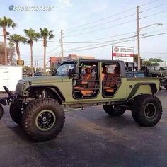 a green jeep with two large tires parked in a parking lot next to palm trees