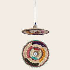 a multicolored circular hanging decoration on a white wall next to a light bulb