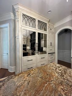 a large marble counter top in a kitchen next to white cupboards and cabinets with glass doors