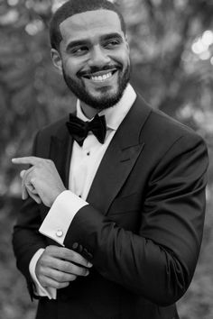 a black and white photo of a man in a tuxedo pointing at something