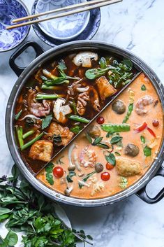 a pan filled with meat and vegetables on top of a table next to chopsticks