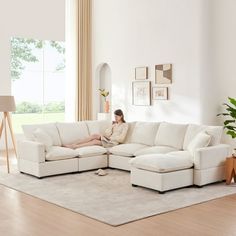 a woman sitting on top of a white couch in a living room next to a window