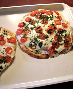 two pizzas with tomatoes on them sitting on a tray