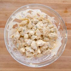 a glass bowl filled with chicken salad on top of a wooden table next to a knife