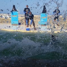 several people in wetsuits standing on the edge of a pier with water splashing over them