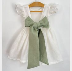 a green and white dress hanging on a wooden hanger with a bow at the neck