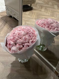 two vases filled with pink flowers sitting on top of a wooden floor next to a mirror