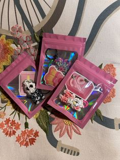 three pink packets with stickers on them sitting on a floral print cloth covered surface