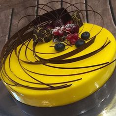 there is a yellow cake with chocolate and berries on the top, sitting on a table