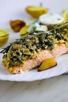 a white plate topped with salmon covered in herbs and lemons next to sliced almonds