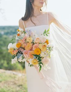 a woman in a white dress holding a bouquet of orange and yellow flowers on her wedding day