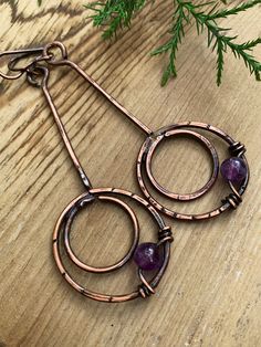 a pair of earrings sitting on top of a wooden table next to a pine tree