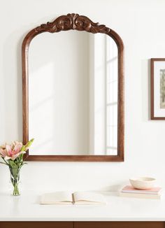 a mirror sitting on top of a dresser next to a vase with flowers in it