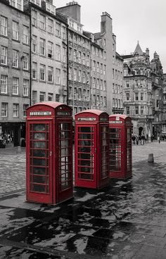 three red telephone booths sitting in the middle of a street with tall buildings behind them