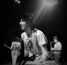 the young man is playing his guitar on stage with other people in the back ground