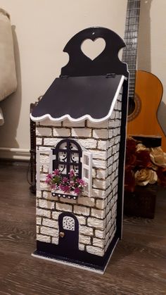 a small house made out of bricks with flowers in the window and guitar behind it