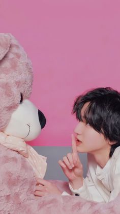 a young man sitting next to a large teddy bear on top of a pink blanket