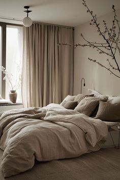 an unmade bed sitting in front of a window next to a vase with flowers