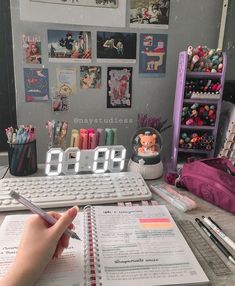 a person is writing on a notebook next to a keyboard and desk with many items