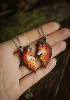 two necklaces that have been made to look like foxes on their faces are shown in the palm of a person's hand