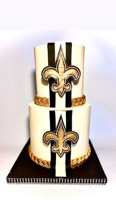 a three tiered cake with black and white designs on it's sides, decorated with gold fleur de lis